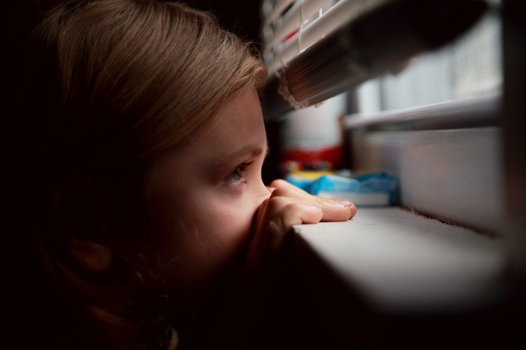 niña mirando por la ventana a través de una persiana veneciana a medida