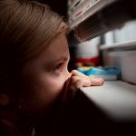 niña mirando por la ventana a través de una persiana veneciana a medida
