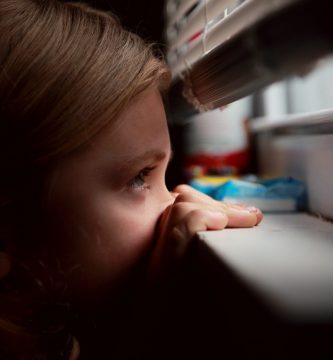 niña mirando por la ventana a través de una persiana veneciana a medida