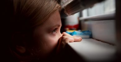 niña mirando por la ventana a través de una persiana veneciana a medida